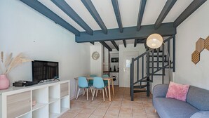 Una sala de estar con sofá, televisión, mesa de comedor, sillas y una escalera.