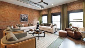 A spacious living room with a brick wall, large windows, and modern furniture. - The Aerie- On Central- LeMars (LeMars)