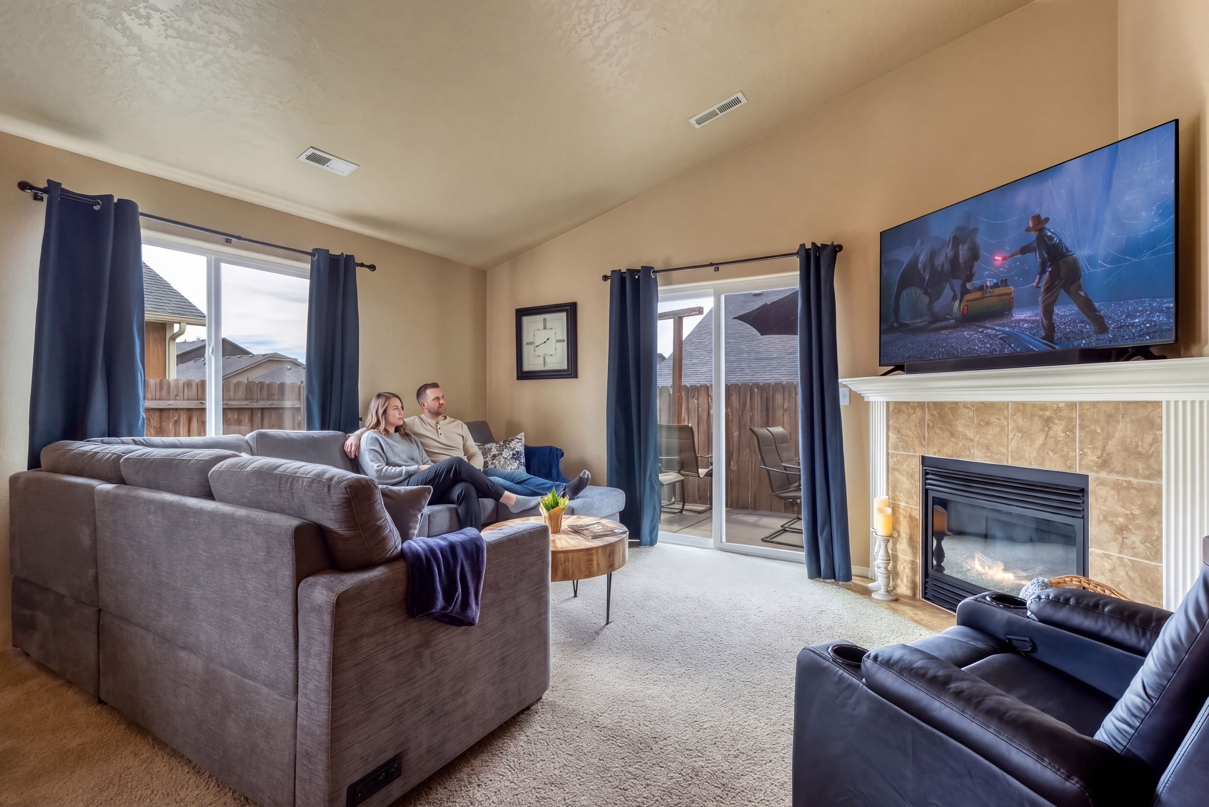 The gas fireplace is lit and the sectional wraps the room, with a large TV above it and recliners opposite. This is where everybody lands once the tasting rooms close: shoes off, fire on, and a bottle from the day finally opened properly.