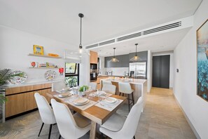 A modern kitchen with a central island, white chairs, and pendant lighting. - Exceptional Beachfront Condo - Allure 105 (Brighton Beach)