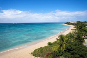 A beach with clear turquoise waters, a sandy shore, and lush greenery. - Exceptional Beachfront Condo - Allure 105 (Brighton Beach)