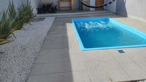 Ett modernt utomhusområde med en pool, en hängmatta, ett litet bord och en dörr som leder ut till en inglasad uteplats.