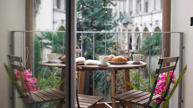 Un balcón con una mesa dispuesta para el desayuno, incluyendo croissants, una taza y un libro abierto.