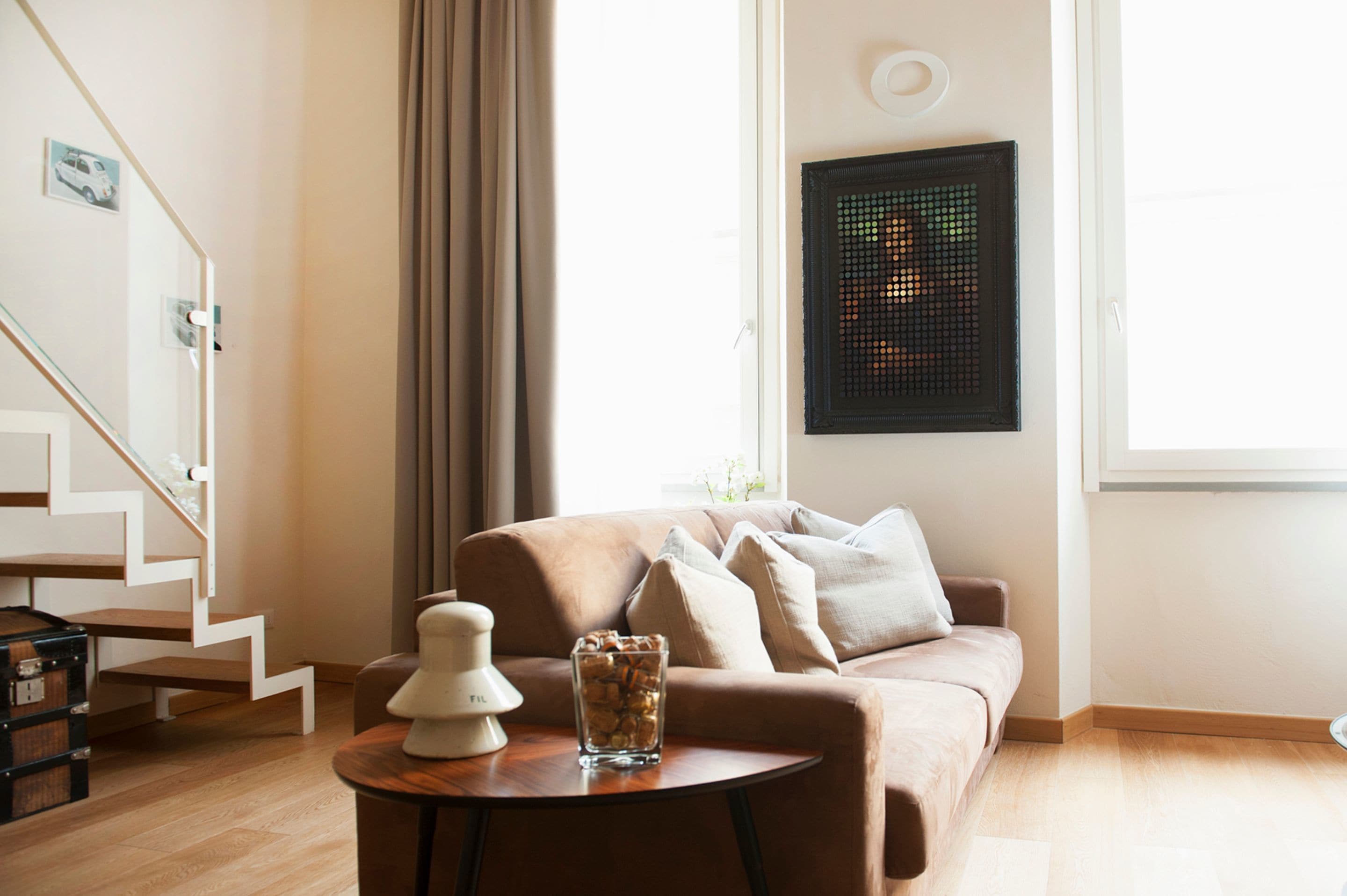 A modern living room with a staircase, a sofa, a small table, and a wall-mounted light fixture.