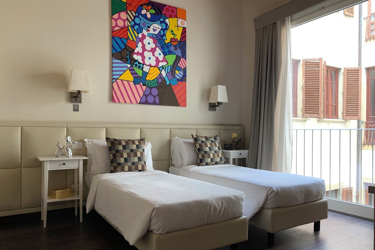 A hotel room with two beds, a painting on the wall, and a balcony with curtains.