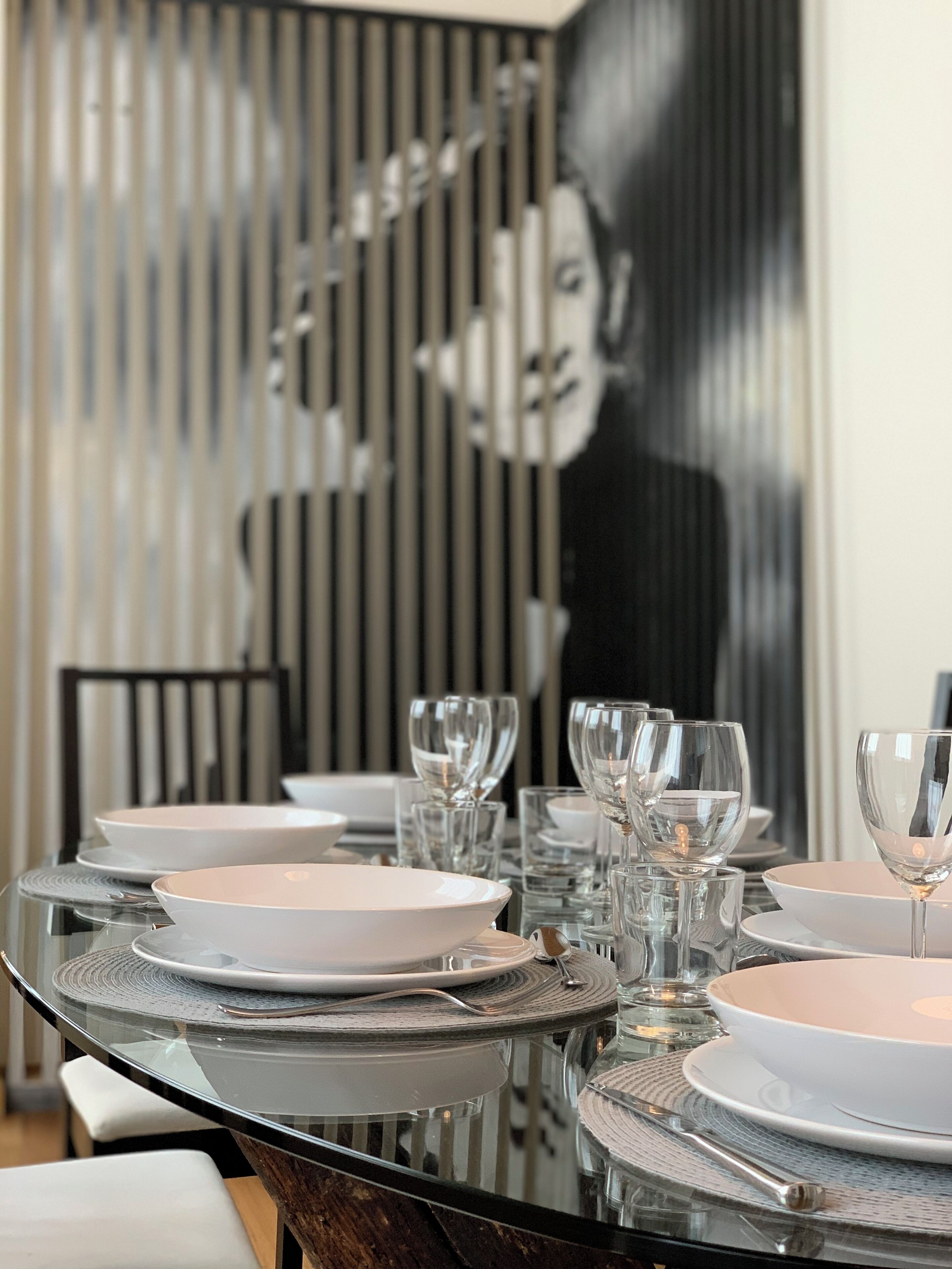 A dining table set with white plates and clear glassware, with a modern, striped wall and a large abstract painting in the background.