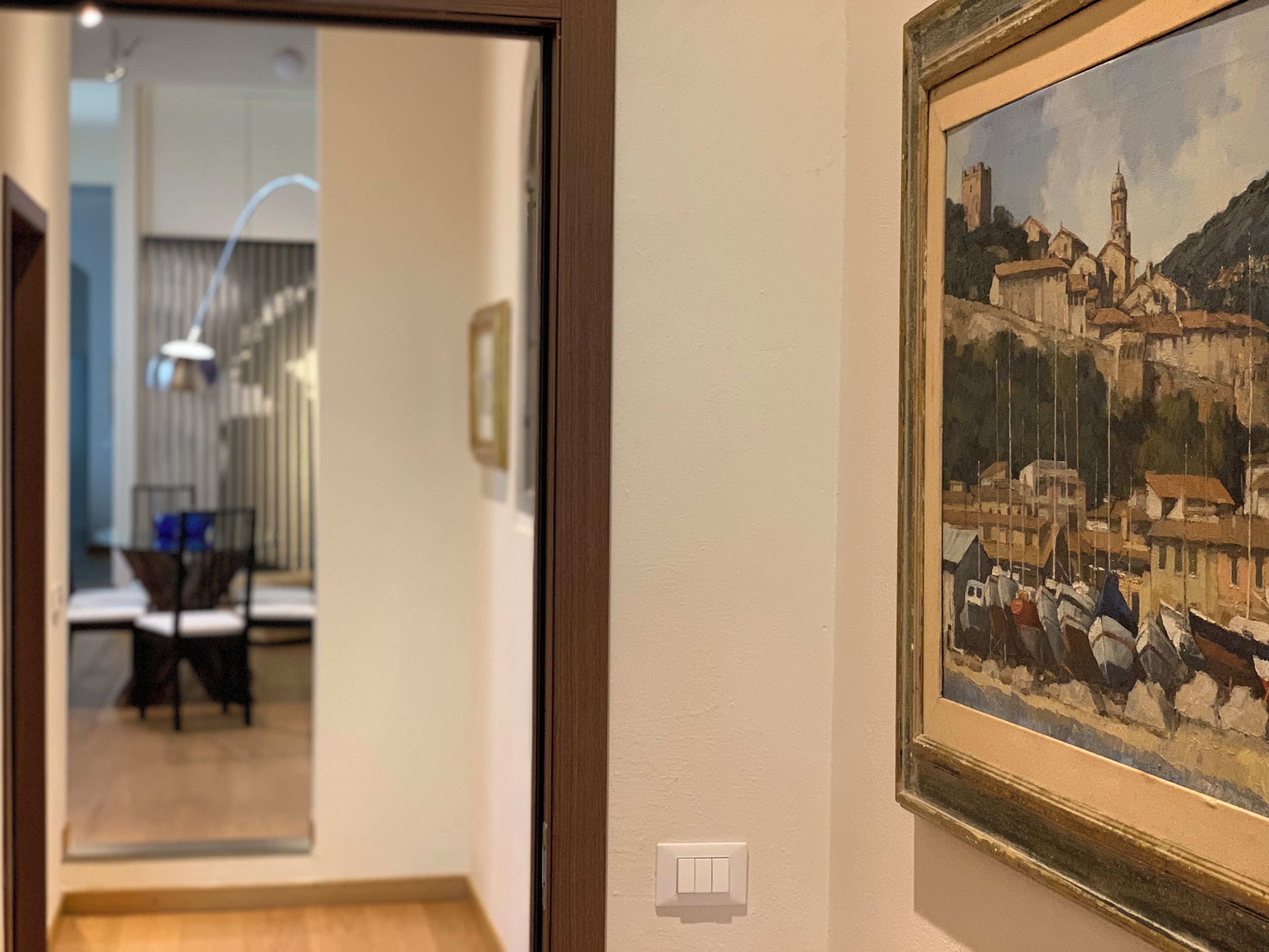 Un couloir orné d’un tableau encadré représentant une ville côtière, une porte donnant sur une salle à manger et un interrupteur sur le mur.