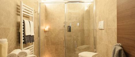 A modern bathroom with a glass-enclosed shower, a white bathtub, and a toilet.