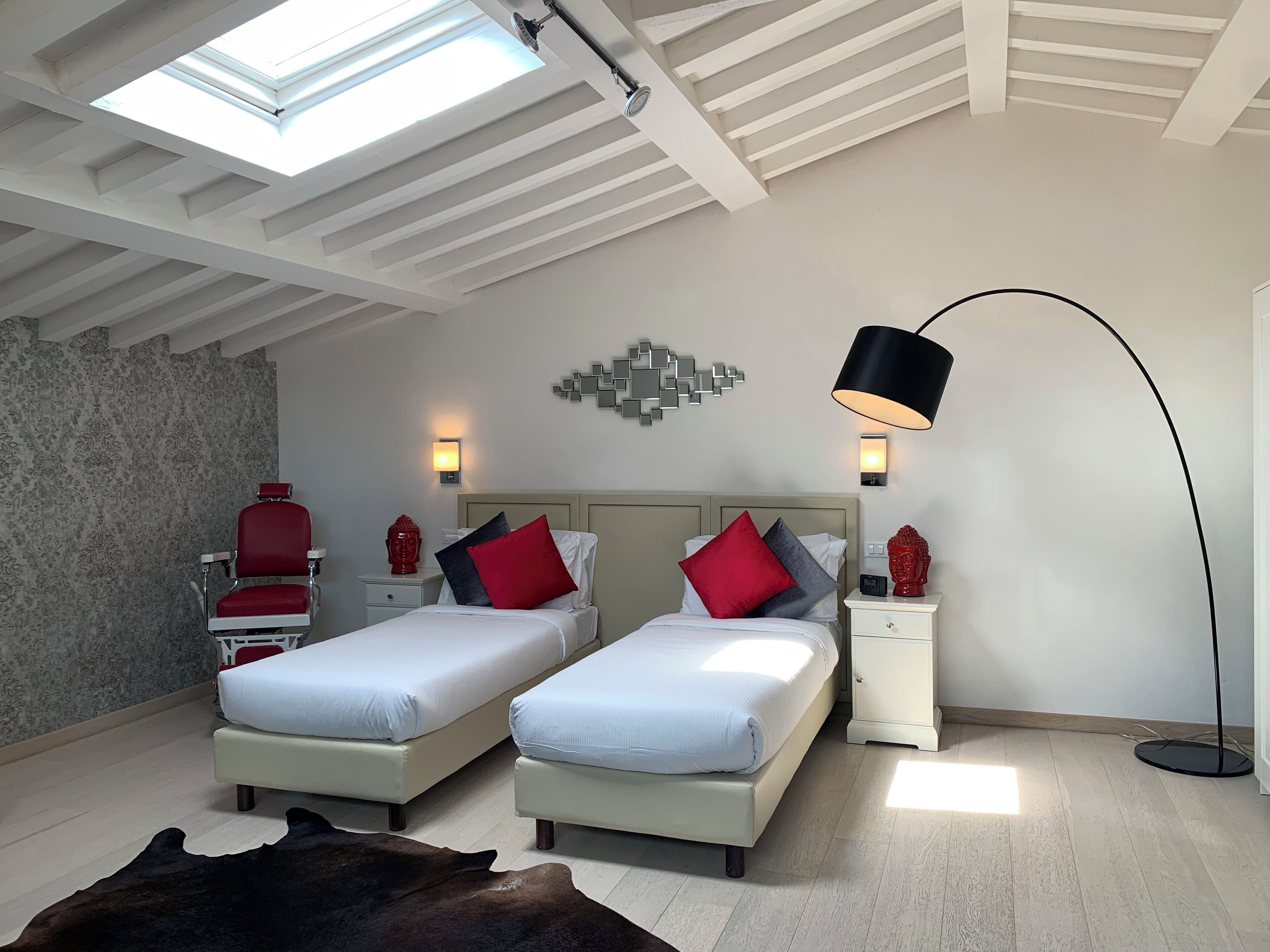 A bedroom with two beds, a skylight, a modern lamp, and a decorative wall piece.