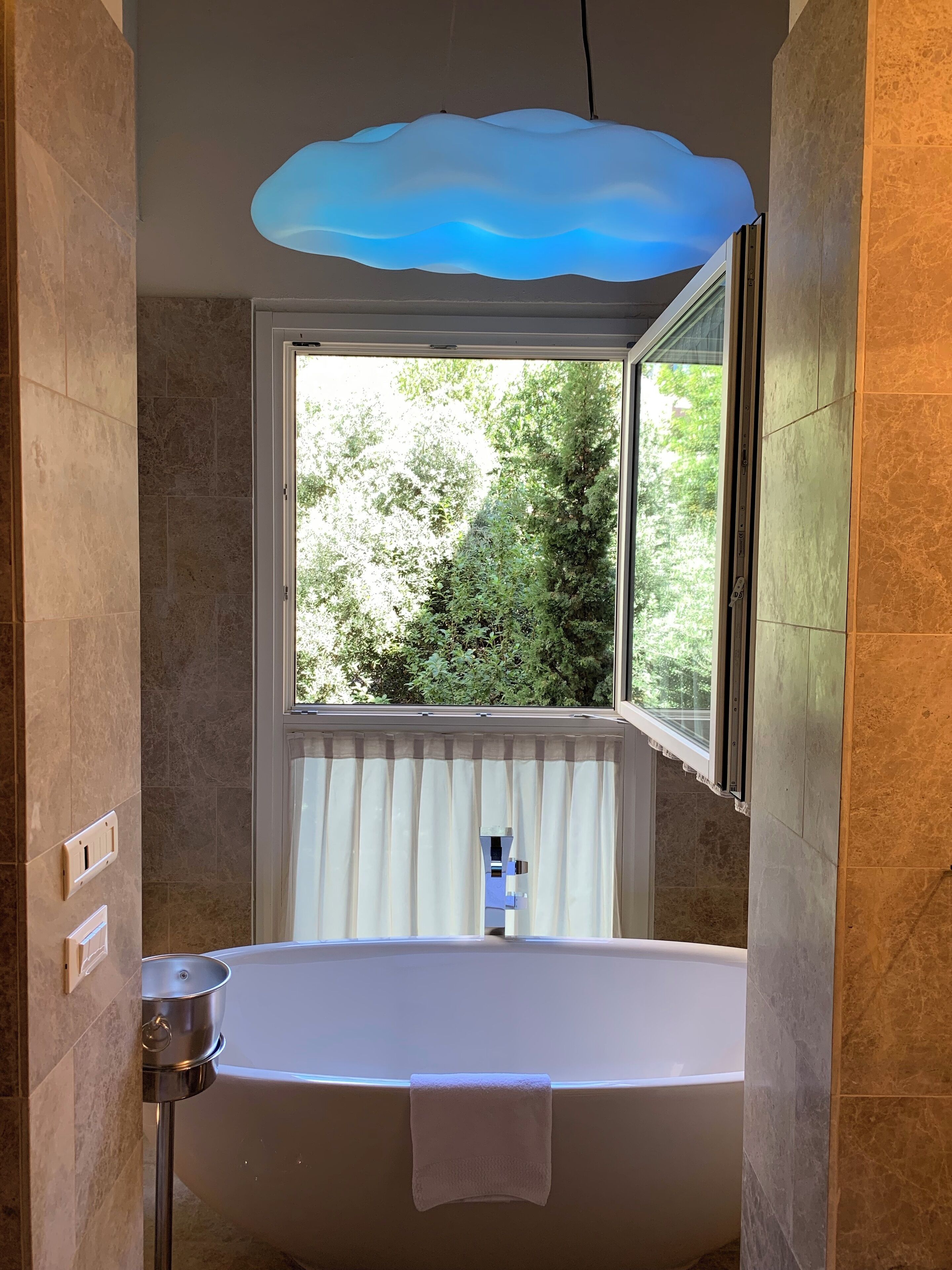 A bathroom with a bathtub, a window with a view of greenery, and a ceiling light fixture.