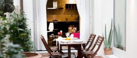 A patio with a table and chairs, a potted plant, and a glimpse of a kitchen in the background.