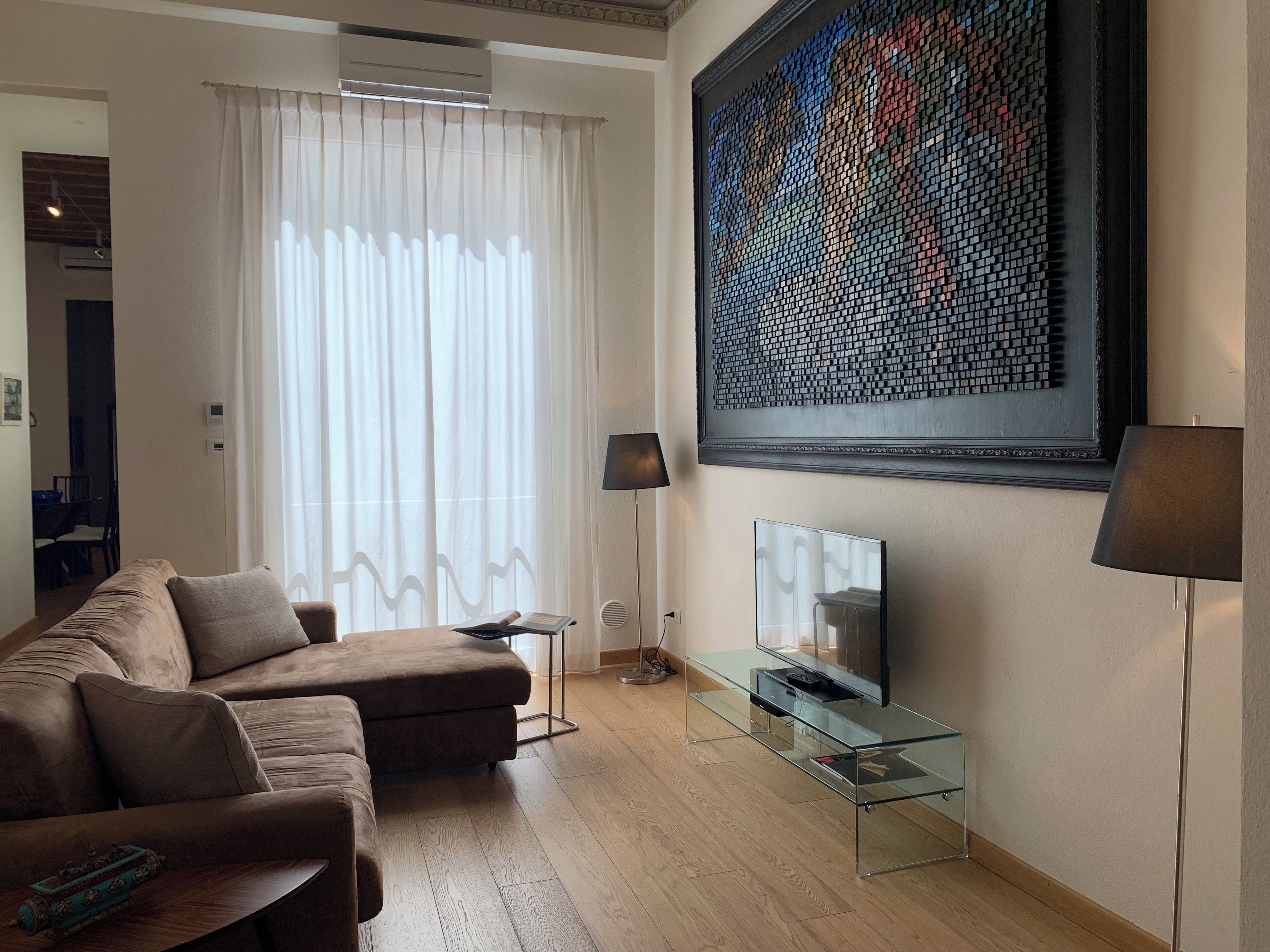 Ein modernes Wohnzimmer mit einer Couch, einem Glastisch, einem Flachbildfernseher und einem großen abstrakten Kunstwerk an der Wand.