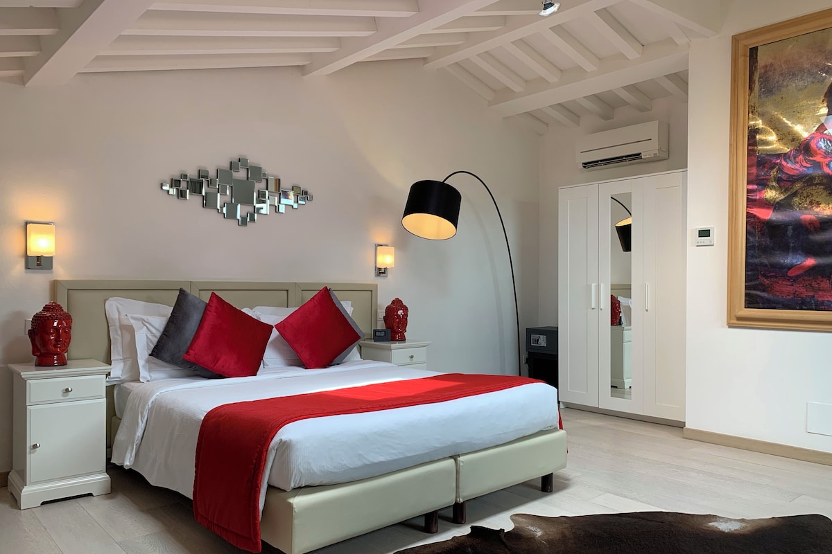 A modern bedroom with a bed, bedside tables, a floor lamp, a decorative wall piece, and a painting.