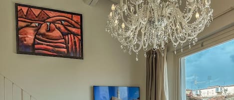 A room with a chandelier, a painting, a chair, a window with a view, and a red vending machine.