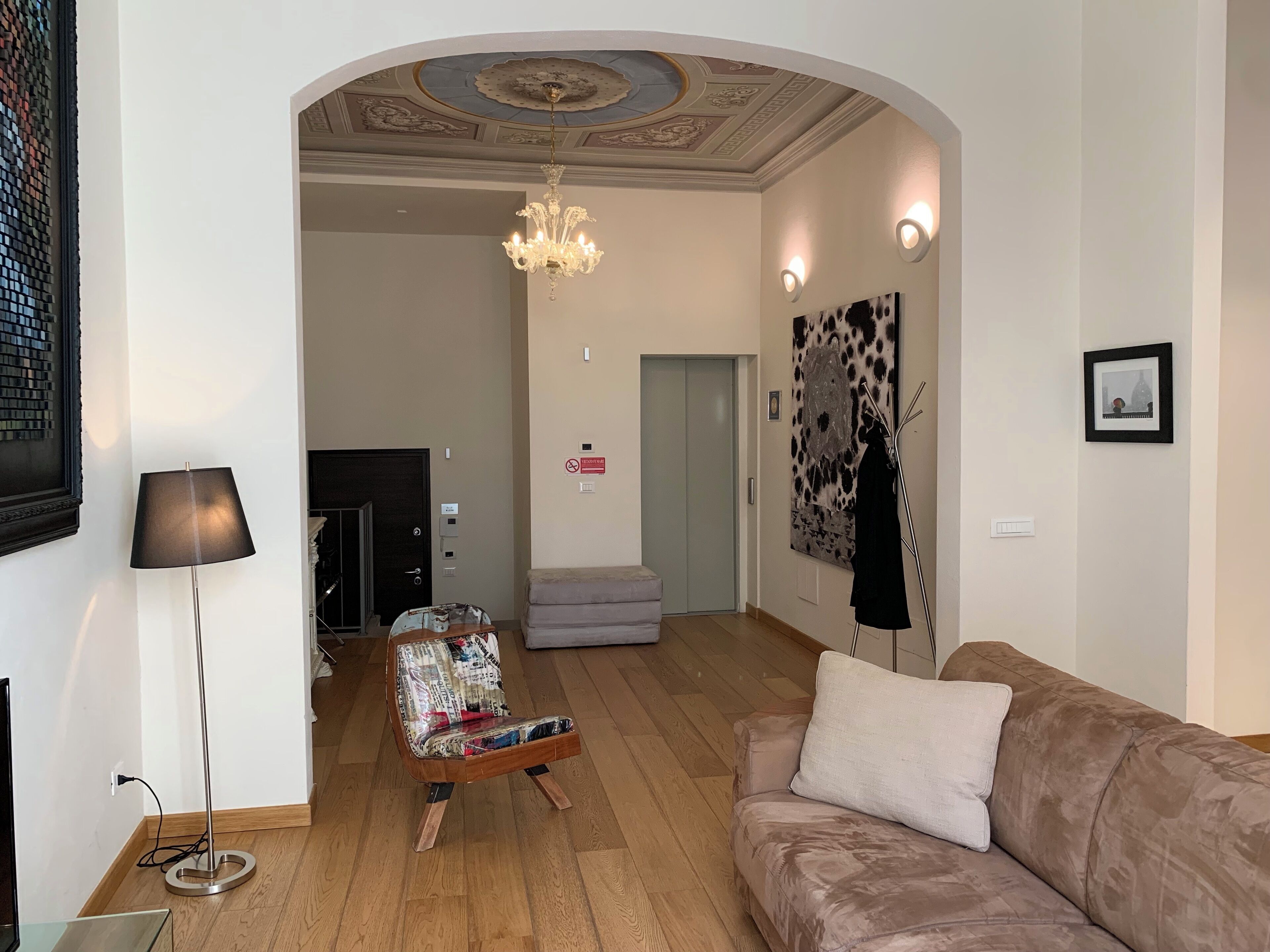 Ett vardagsrum med en kristallkrona, en soffa, en golvlampa och en mönstrad fåtölj.