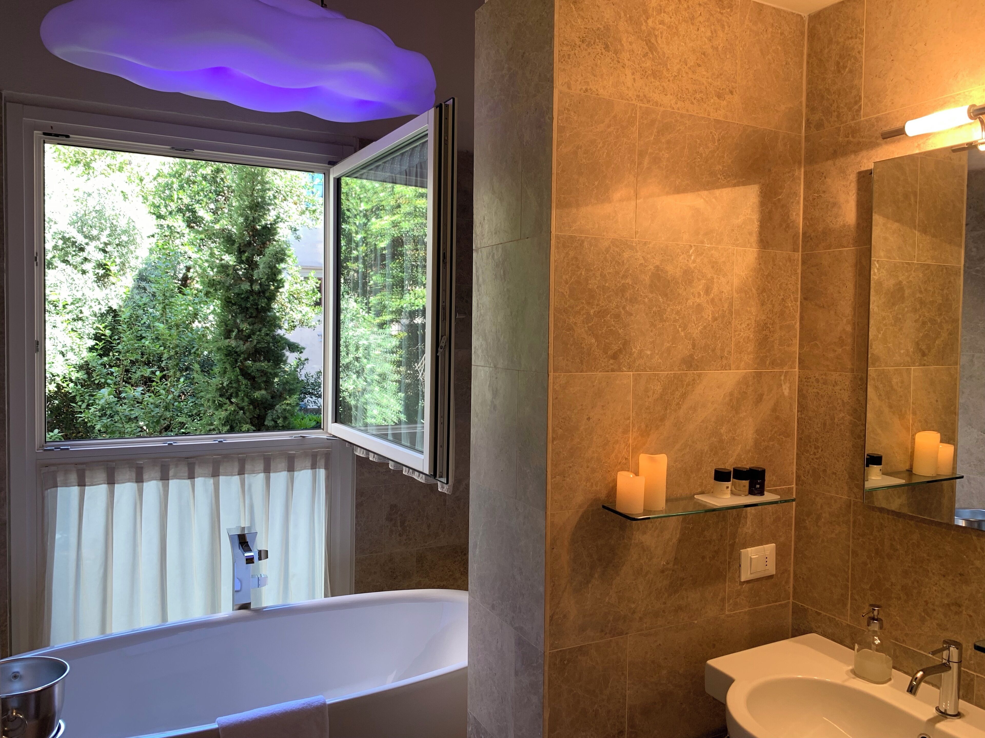 Ein Badezimmer mit einer Badewanne, einem Waschbecken, einem Spiegel und einem Fenster mit Blick auf Grünflächen.