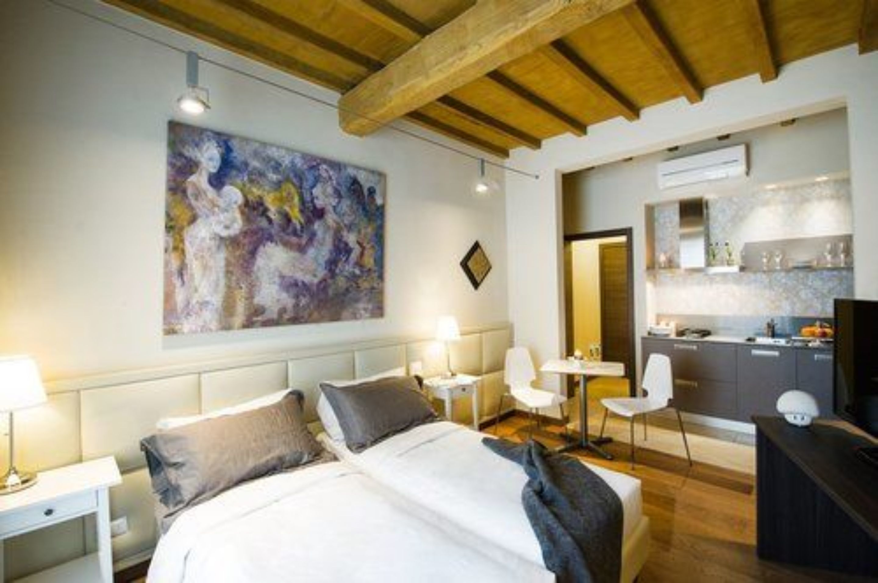 A modern hotel room with a large bed, a desk, a chair, and a painting on the wall.