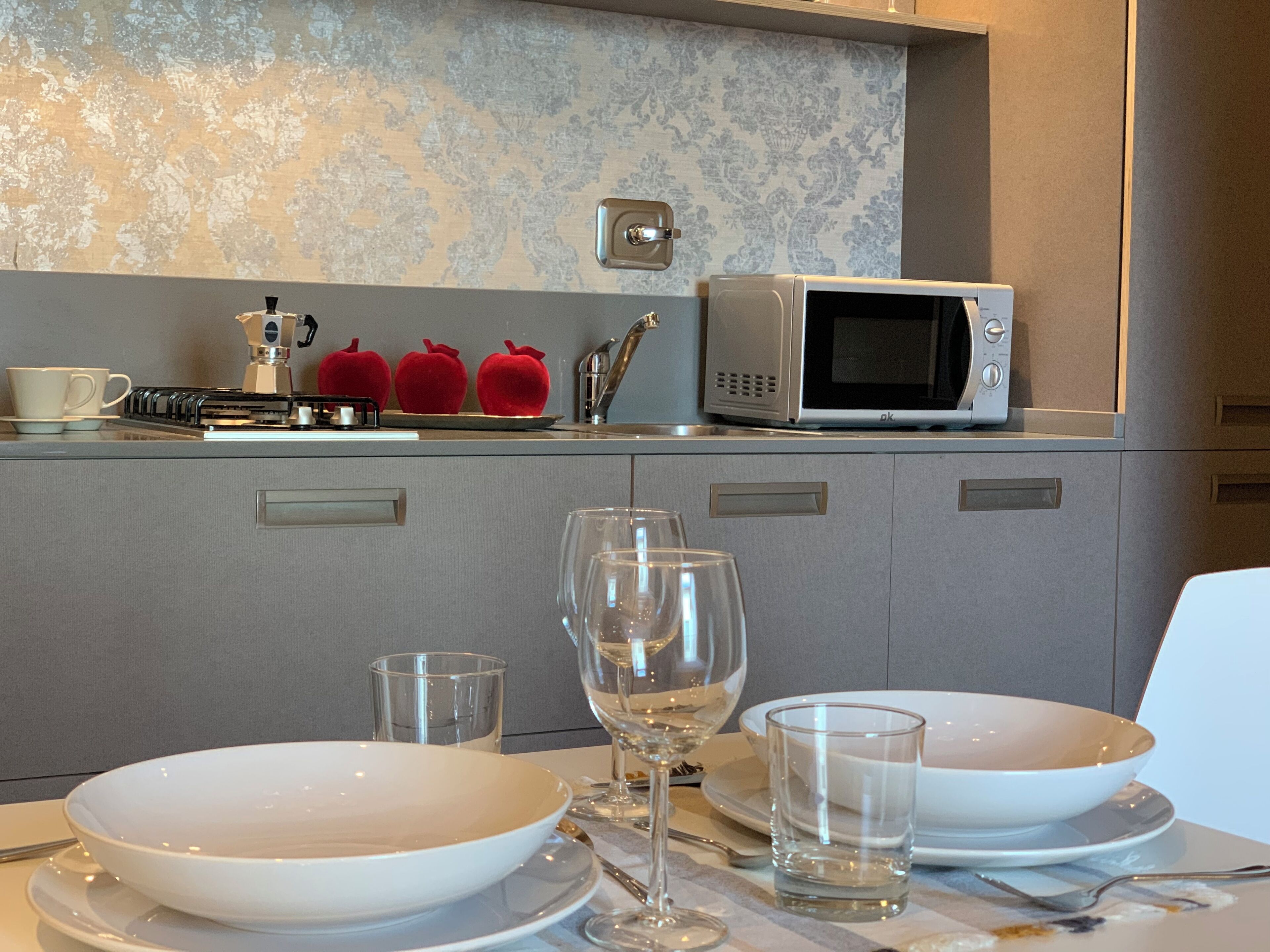 Una cocina moderna con microondas, tetera y una mesa de comedor dispuesta con platos, vasos y cubiertos.
