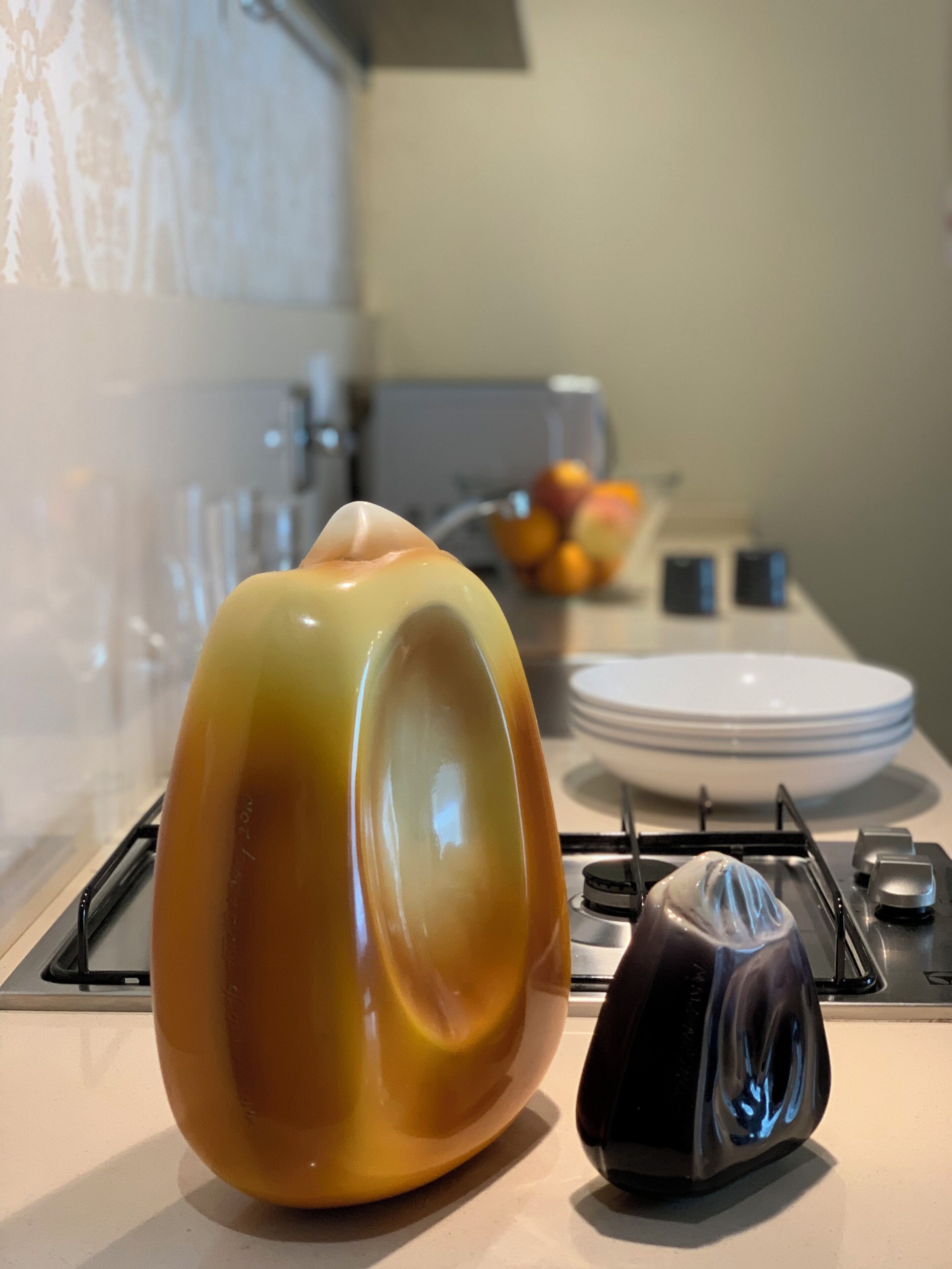 Un piano di lavoro della cucina con un oggetto ceramico grande, lucido e ovale, un oggetto scuro più piccolo e una pila di piatti bianchi.