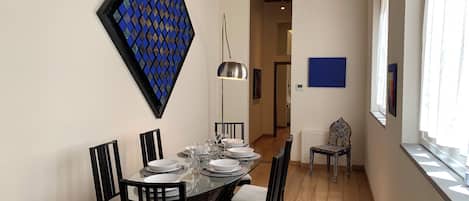 A dining area with a glass table, black chairs, and a blue patterned wall decoration.