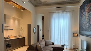 Una sala de estar moderna con un sofá, una mesita, un televisor y una zona de cocina con estufa y armarios.