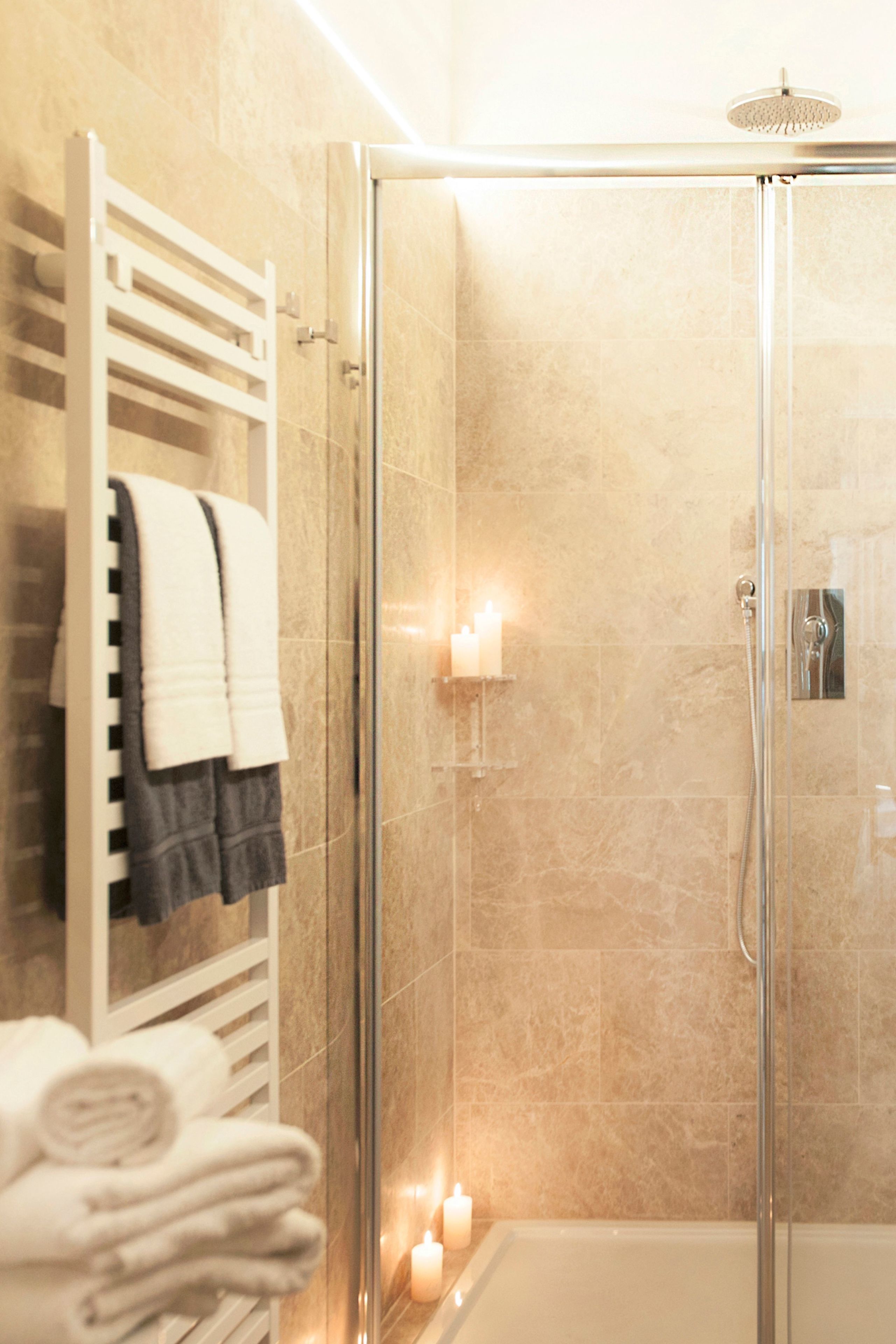Ein modernes Badezimmer mit einer gläsernen Duschkabine, einem weißen Handtuchhalter mit gefalteten Handtüchern und einer Kerze auf dem Boden.