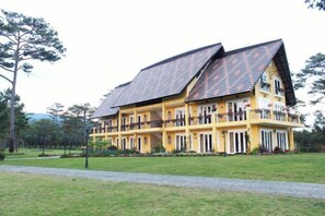 A large yellow building with a sloped roof, multiple balconies, and a paved walkway in front. - Binh An Village Dalat Resort (Da Lat)