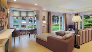 A modern hotel room with a sofa, dining table, chairs, and a view of a garden. - Binh An Village Dalat Resort (Da Lat)