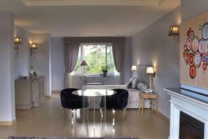A living room with a fireplace, a dining area with a round table, and a view of the outdoors. - Binh An Village Dalat Resort (Da Lat)