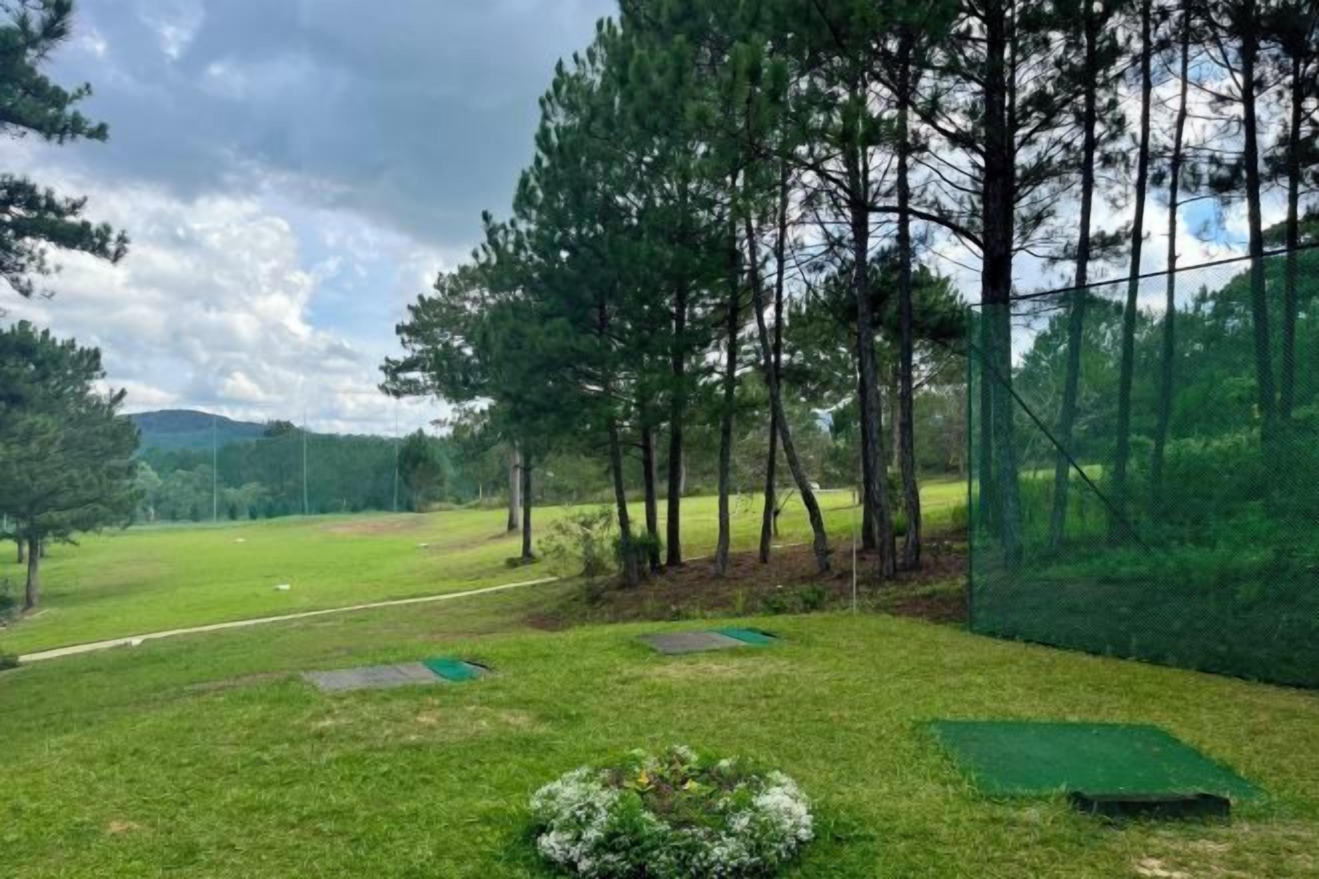 A golf course with trees, a netted area, and a green field.