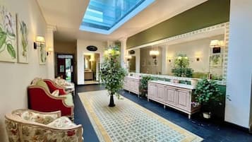 A hotel lobby with a central seating area, a reception desk, a large mirror, and a plant.