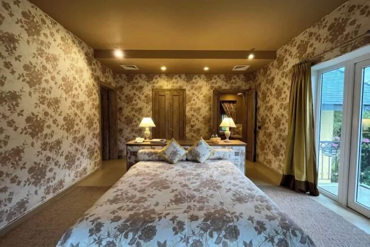 A bedroom with floral wallpaper, a large bed, two bedside tables with lamps, and a window with curtains.