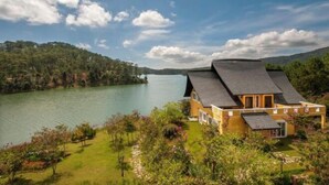 A house with a sloped roof overlooking a lake, surrounded by lush greenery and hills. - Binh An Village Dalat Resort (Da Lat)