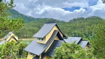 A yellow building with a steep roof, surrounded by trees and a lake.