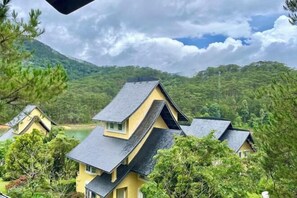 A yellow building with a steep roof, surrounded by trees and a lake. - Binh An Village Dalat Resort (Da Lat)