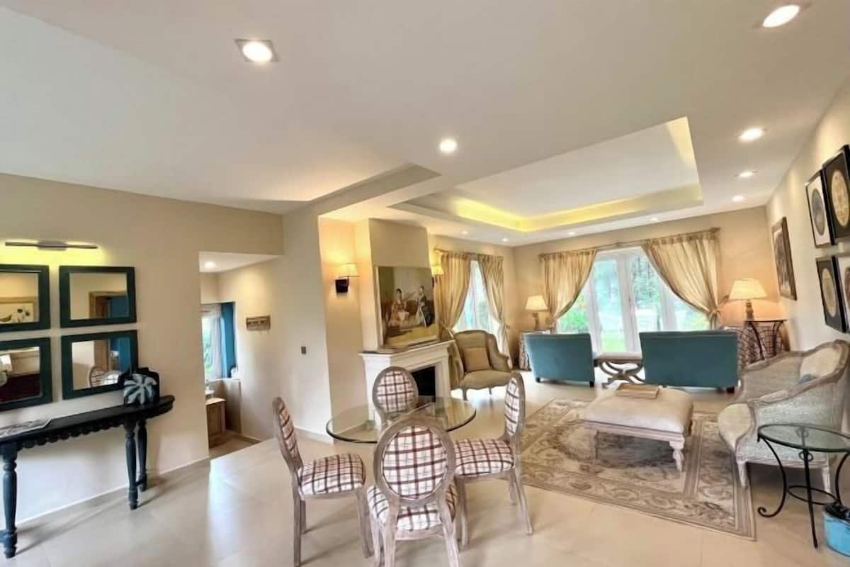 A spacious living room with a fireplace, a dining area with a glass table, and a seating area with sofas and chairs.