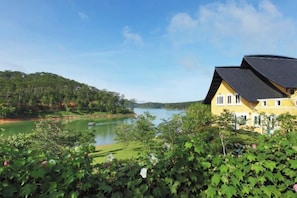 A yellow building with a dark roof, a lake, and a forested hillside. - Binh An Village Dalat Resort (Da Lat)