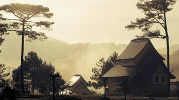 A traditional house with a thatched roof, surrounded by trees and a misty background.