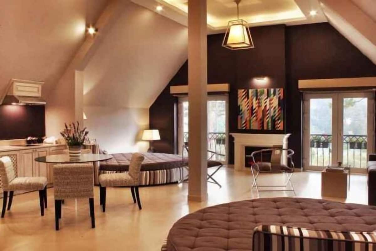 A spacious living area with a round seating arrangement, a fireplace, and a large window providing a view of the outdoors.