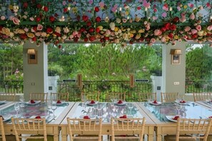 An indoor dining area with a glass table and chairs, surrounded by a decorative floral canopy, with a view of greenery outside. - Binh An Village Dalat Resort (Da Lat)