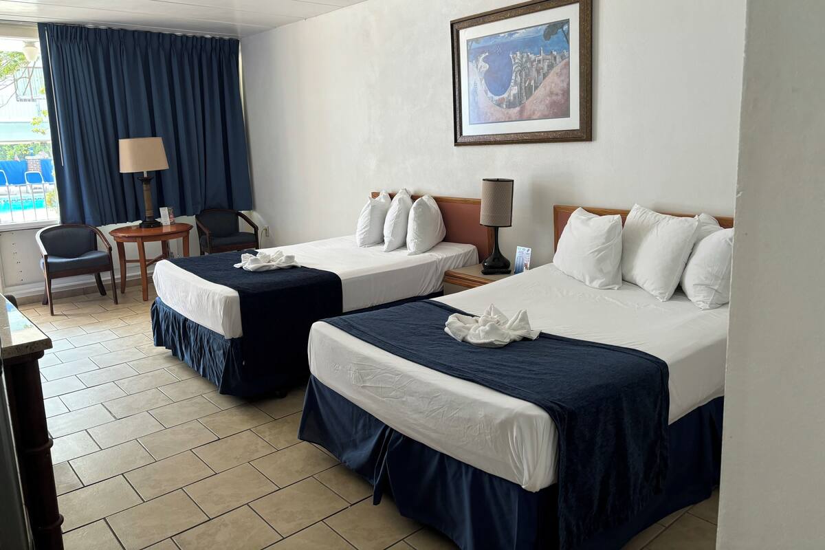 Una habitación de hotel con dos camas, un escritorio, una silla, una lámpara y un cuadro en la pared.
