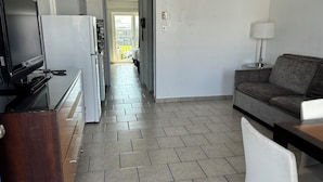 Cocina moderna con refrigerador, estufa y microondas. Se observa un comedor con sofá y lámpara.