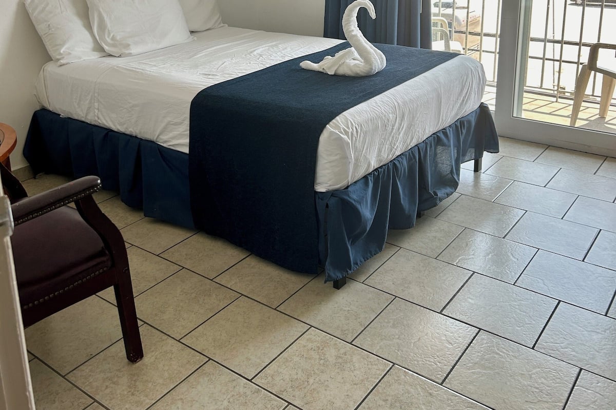 Habitación de hotel con una cama, una silla, un ventanal con vista a un puerto deportivo y un cuadro en la pared.