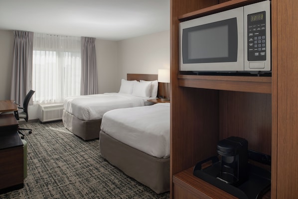 Habitación de hotel con dos camas, un escritorio, una silla, una cafetera y un microondas.