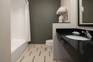 Ein modernes Badezimmer mit Badewanne, Toilette und Waschtisch mit Waschbecken und Spiegel.