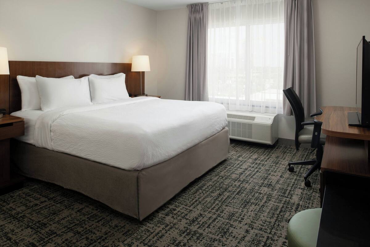 A hotel room with a large bed, a desk, a chair, and a window with curtains.