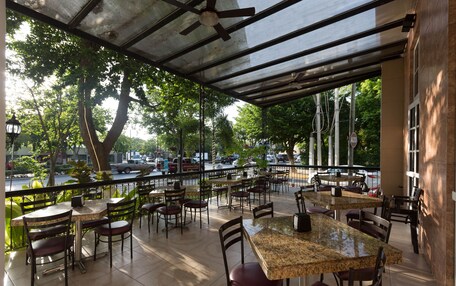 An outdoor cafe with tables and chairs, a covered area, and a view of the street and trees.