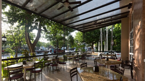 An outdoor cafe with tables and chairs, a covered area, and a view of the street and trees. - Hotel Victoria Merida (Mérida)