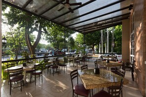 An outdoor cafe with tables and chairs, a covered area, and a view of the street and trees. - Hotel Victoria Merida (Mérida)