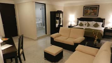 A hotel room with a bed, a sofa, a dining table with chairs, and a bathroom visible through an open door.
